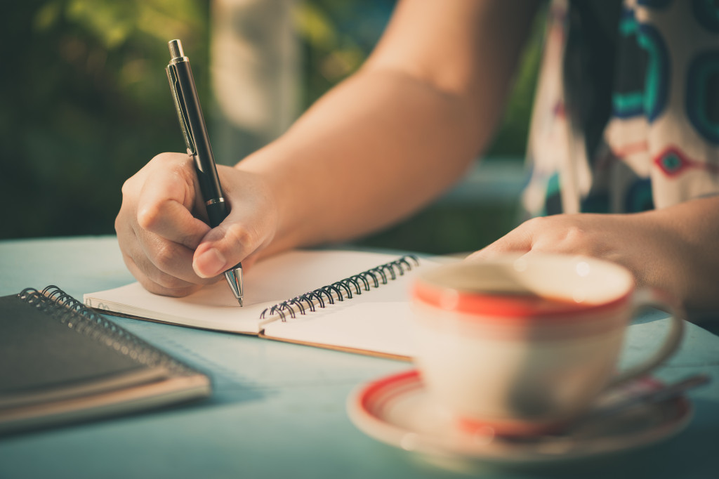 Woman writes on a notebook while having coffee