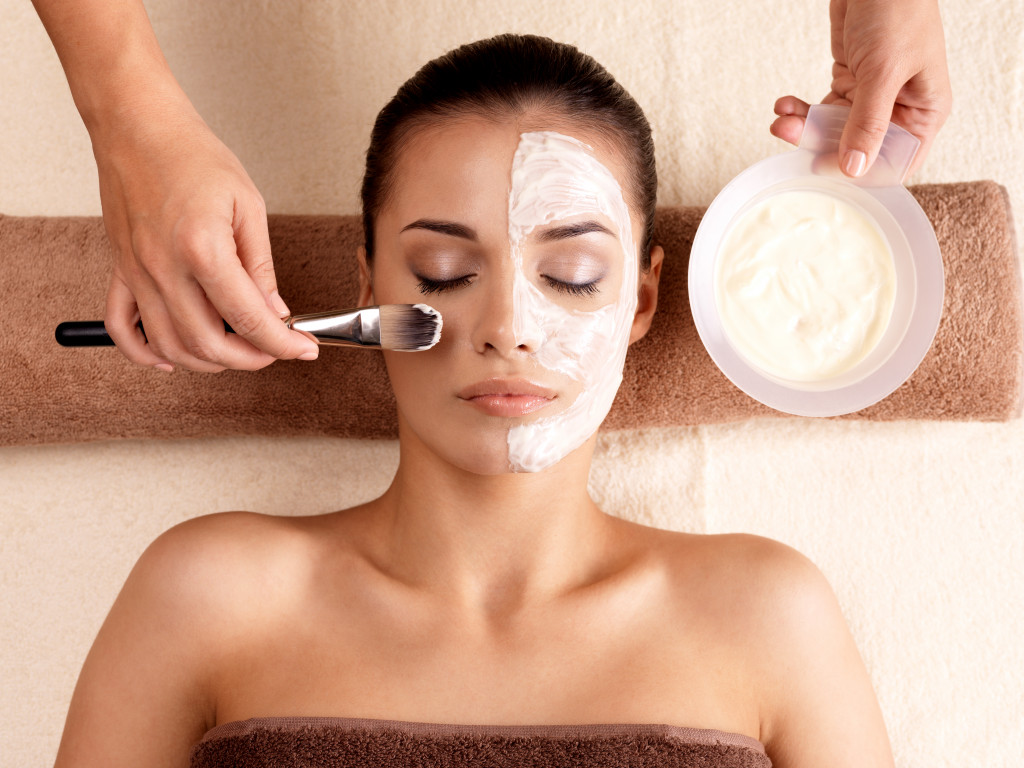 woman with eyes closed applying facial cream in her face in a spa