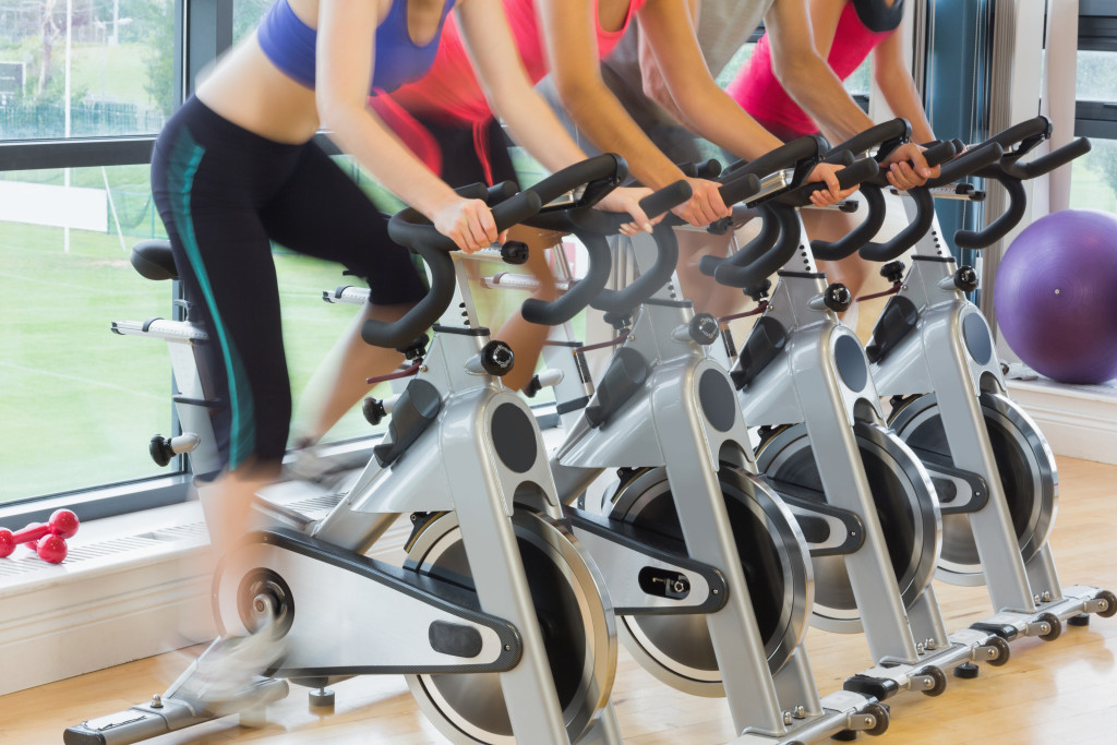 Four people exercising using a stationary bike at a gym.