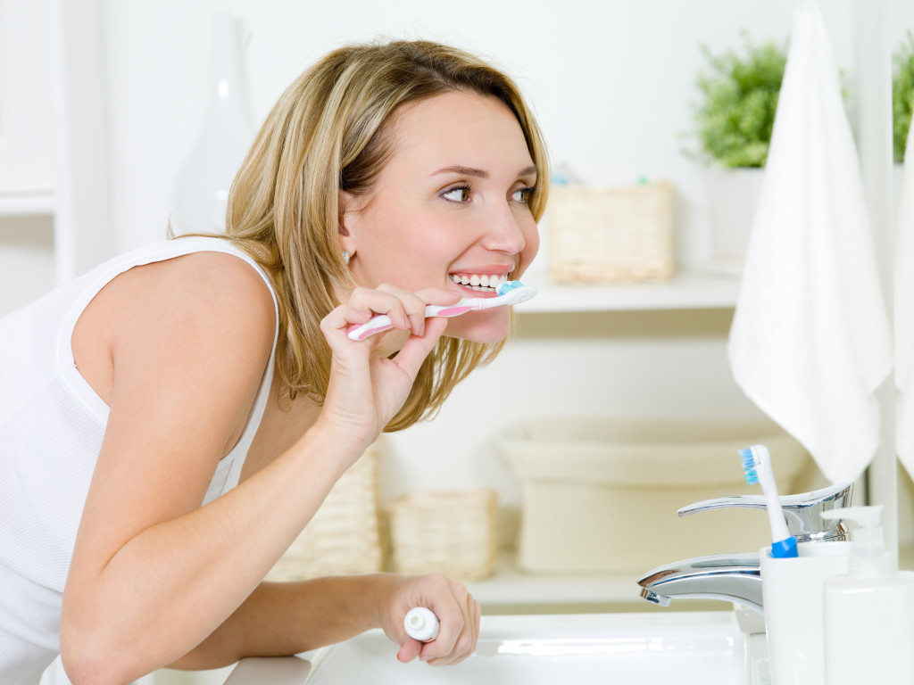 woman smiling while brushing teeth in the sink